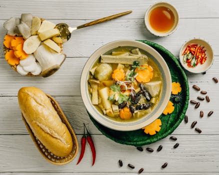 A bowl of soup with bread and vegetables on a white table